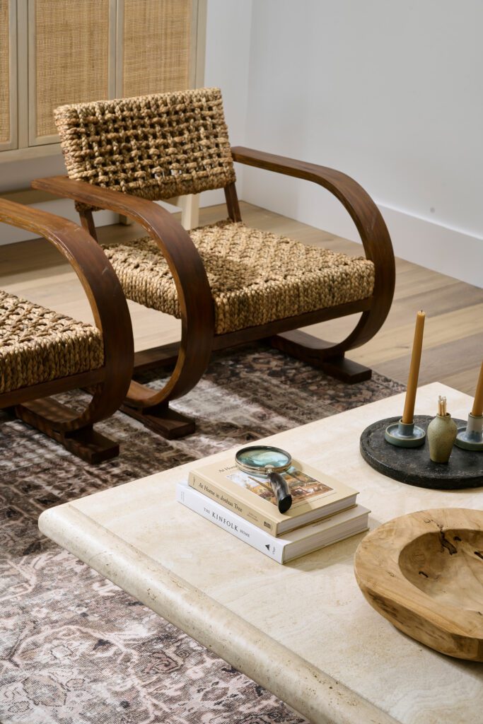 Curved sculptural wood chair with woven seat beside a stone coffee table styled with books, candles, and organic decor.