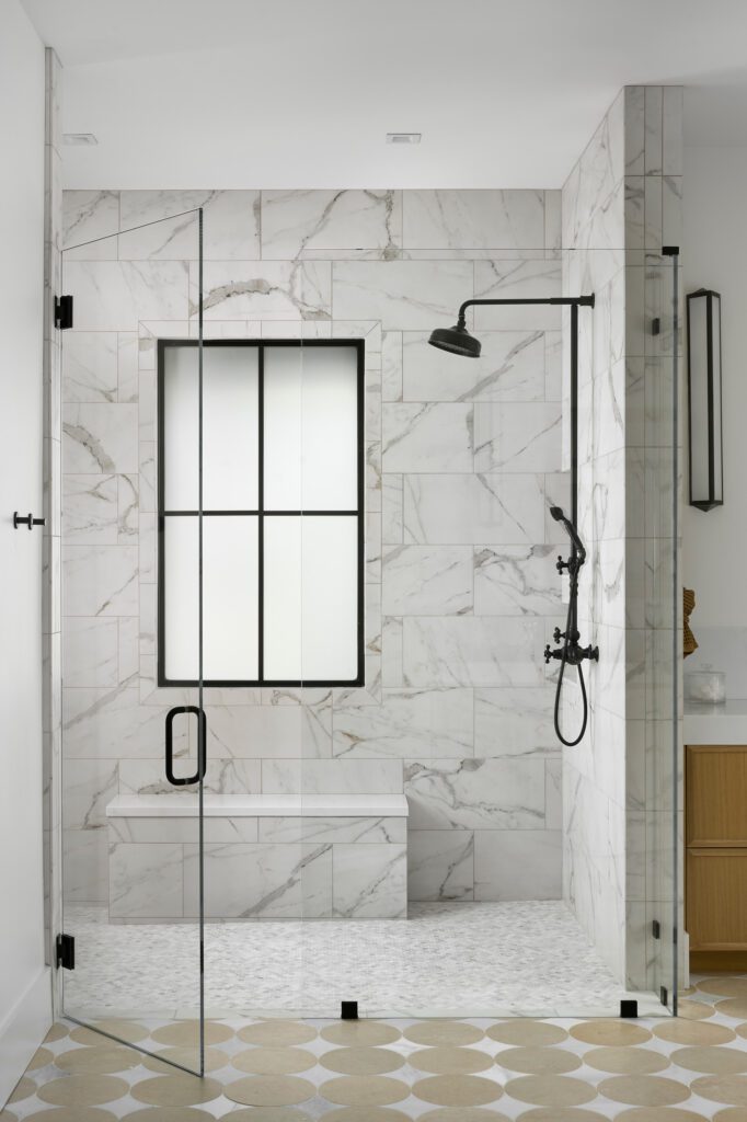 Luxury marble walk-in shower with black framed glass enclosure, modern fixtures, and natural stone walls.