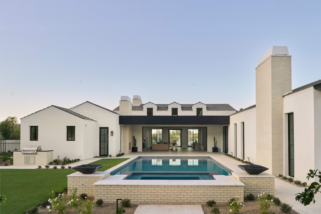 Luxury desert home exterior with illuminated pool and large glass doors opening to the living area, designed for entertaining in Arizona.