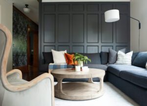 Modern living room with navy paneled wall, curved wood coffee table, and a deep sectional accented by mixed pillows and sculptural decor.