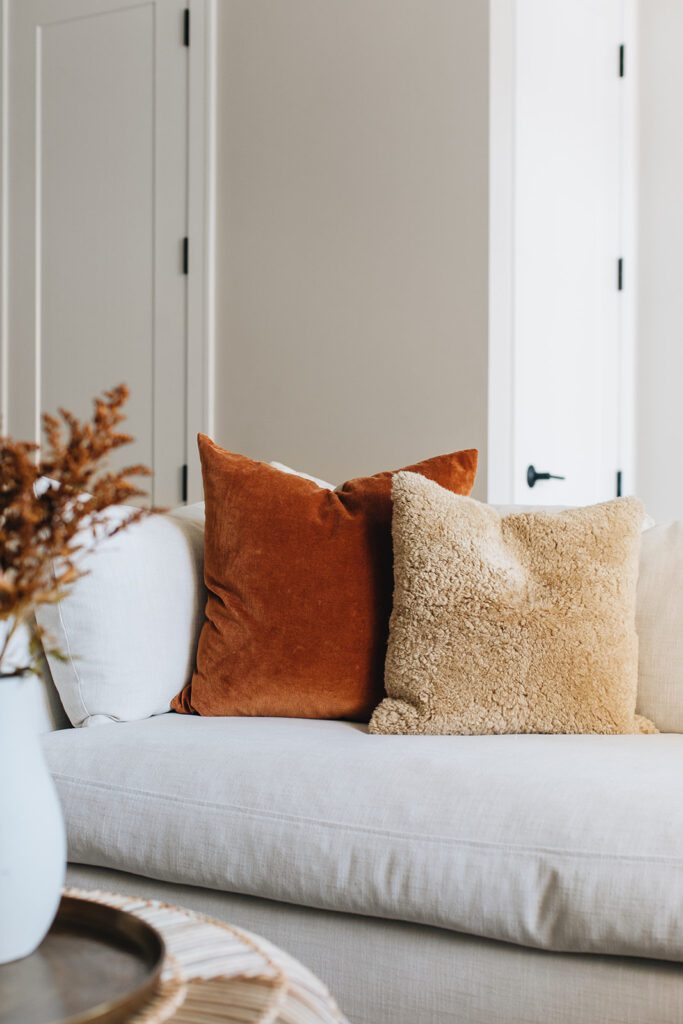 Close-up of a white sofa with rust velvet and beige boucle pillows styled in a neutral living space.