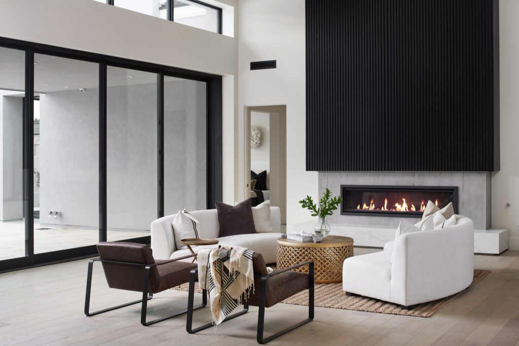 Minimalist living room with white armchairs, brown leather sling chairs, modern fireplace, and sculptural side tables in a neutral desert palette.