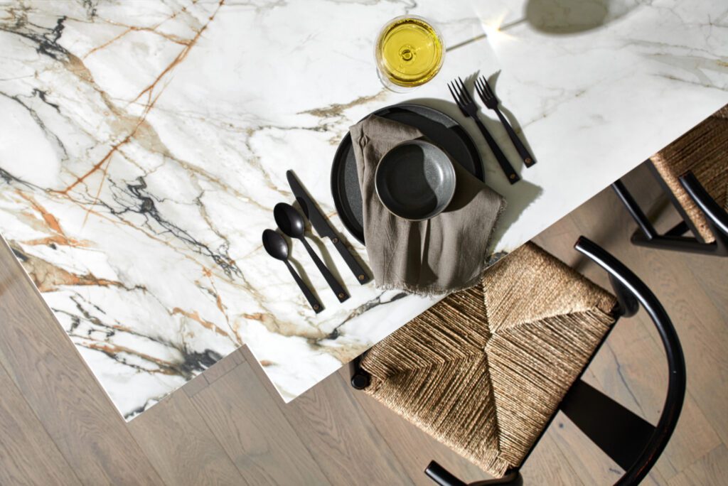 Overhead view of a marble dining table set with black flatware, neutral dishware, and a woven seat dining chair.