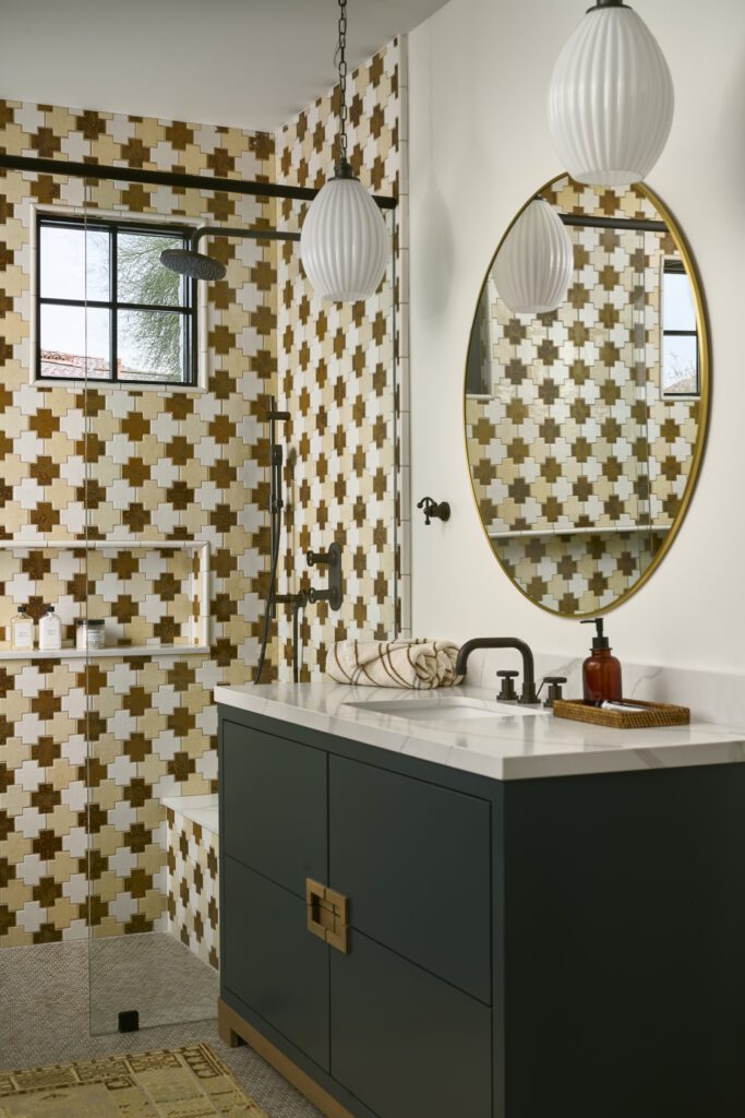 Luxury bathroom with a freestanding tub, green vanity, patterned tile accent wall, brass fixtures, and layered lighting, showcasing a refined and cohesive interior design.