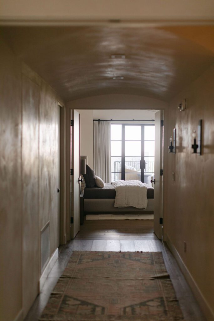 Warm modern hallway with natural wood walls, textured flooring, and a cozy seating area framed by soft natural light.