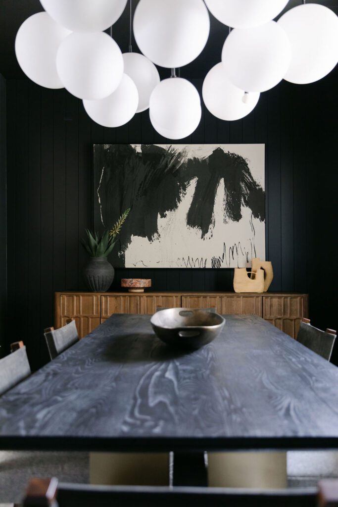 Dining space with black shiplap wall, light wood credenza, and oversized black-and-white abstract painting.