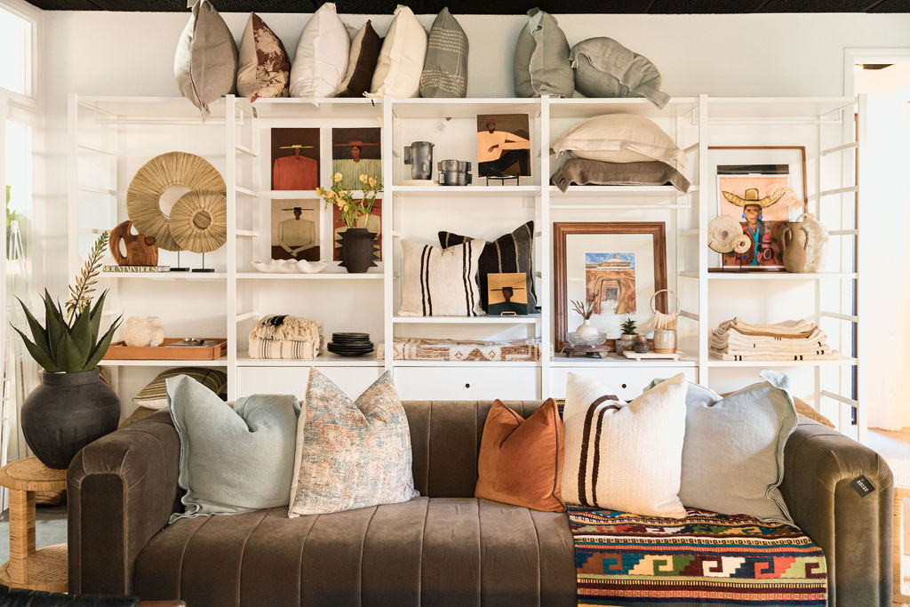 Textural throw pillows on a deep brown sofa in front of a curated Atelier shelving wall styled with vintage finds, books, and sculptural accessories.