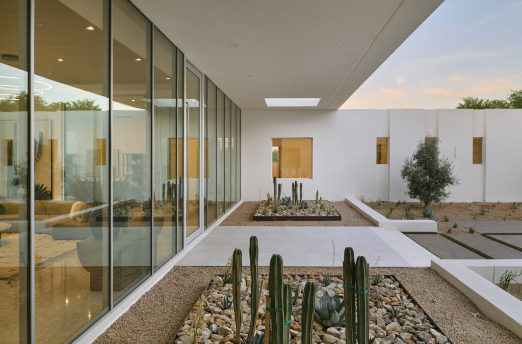 An ultra-modern interior space looking out through tall, expansive glass panels onto a minimalist courtyard filled with cacti and gravel, creating a strong indoor-outdoor visual connection.
