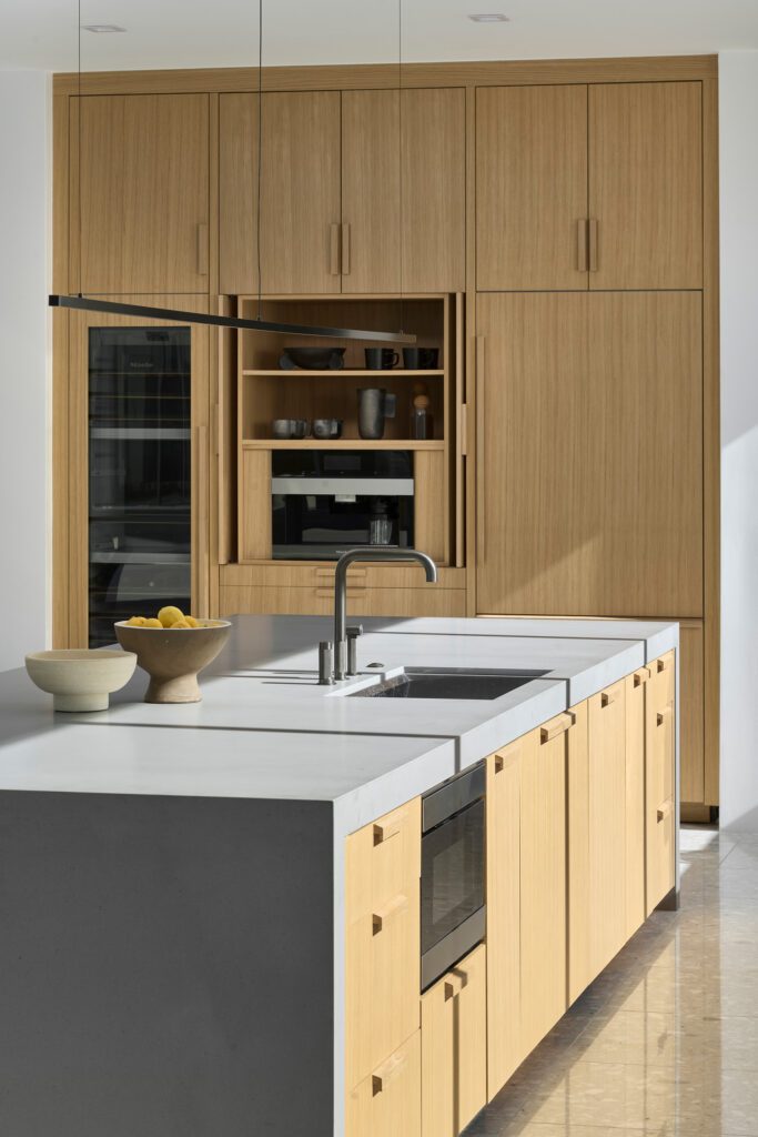 Luxury kitchen featuring custom white oak cabinetry, a waterfall island, integrated appliances, and warm modern finishes.