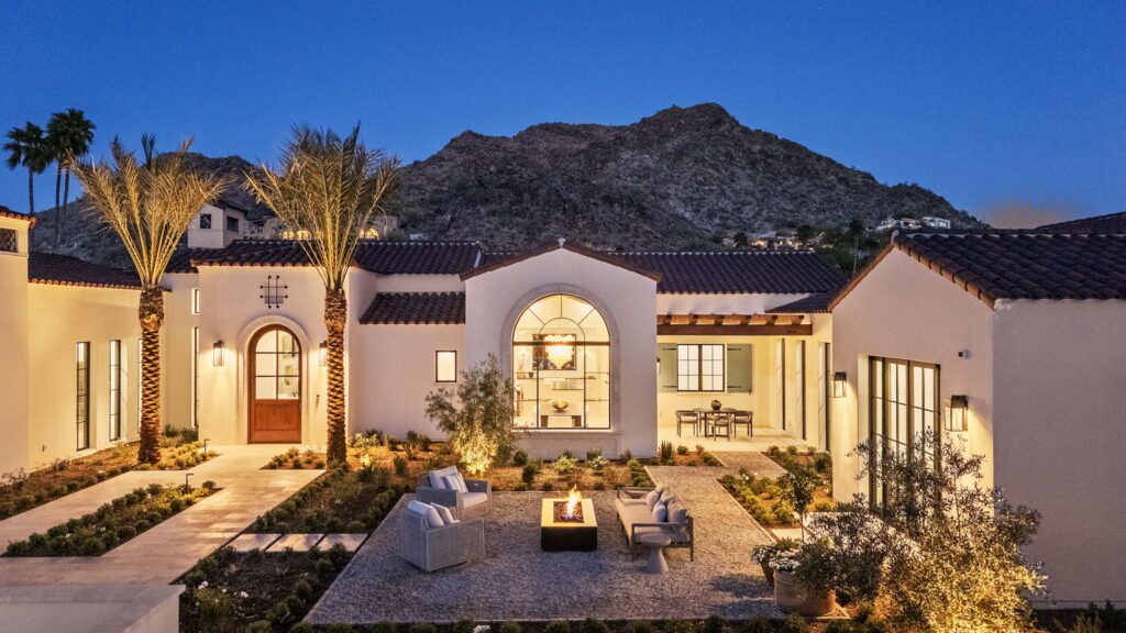Luxury desert home in Paradise Valley at dusk with mountain views, warm exterior lighting, and a central firepit seating area designed for connection and entertaining.