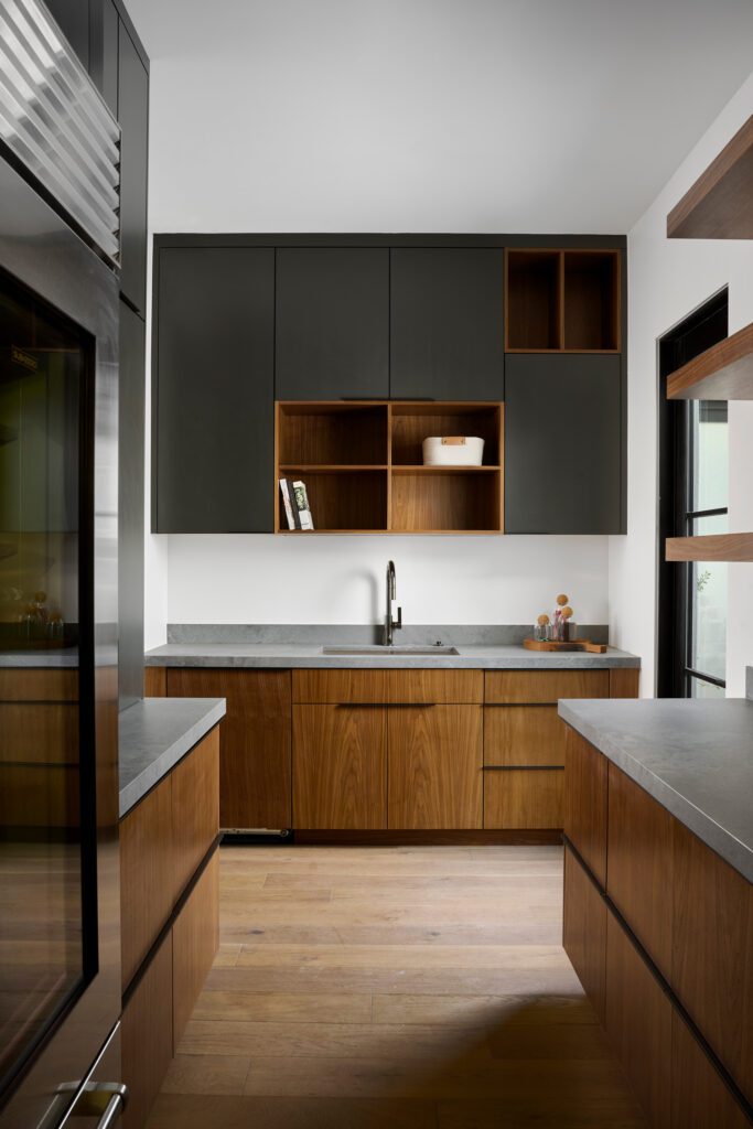 Modern butler’s pantry with walnut cabinetry, charcoal countertops, and open shelving designed for functional elegance in a luxury desert home.