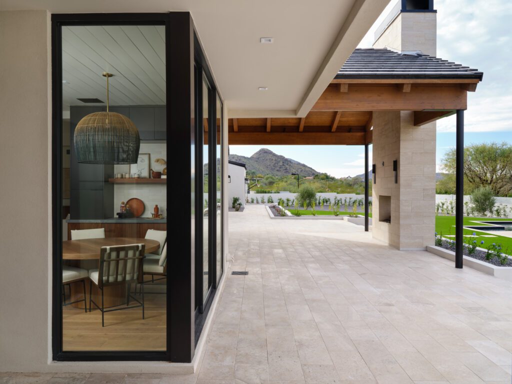 View from patio into a modern breakfast nook with a woven pendant and round wood table in a luxury Scottsdale home with mountain views.