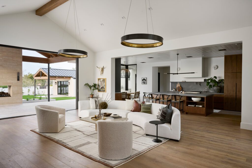 Open-concept living room with neutral curved sofa, warm wood floors, and expansive views to the outdoor patio in a Scottsdale desert home.