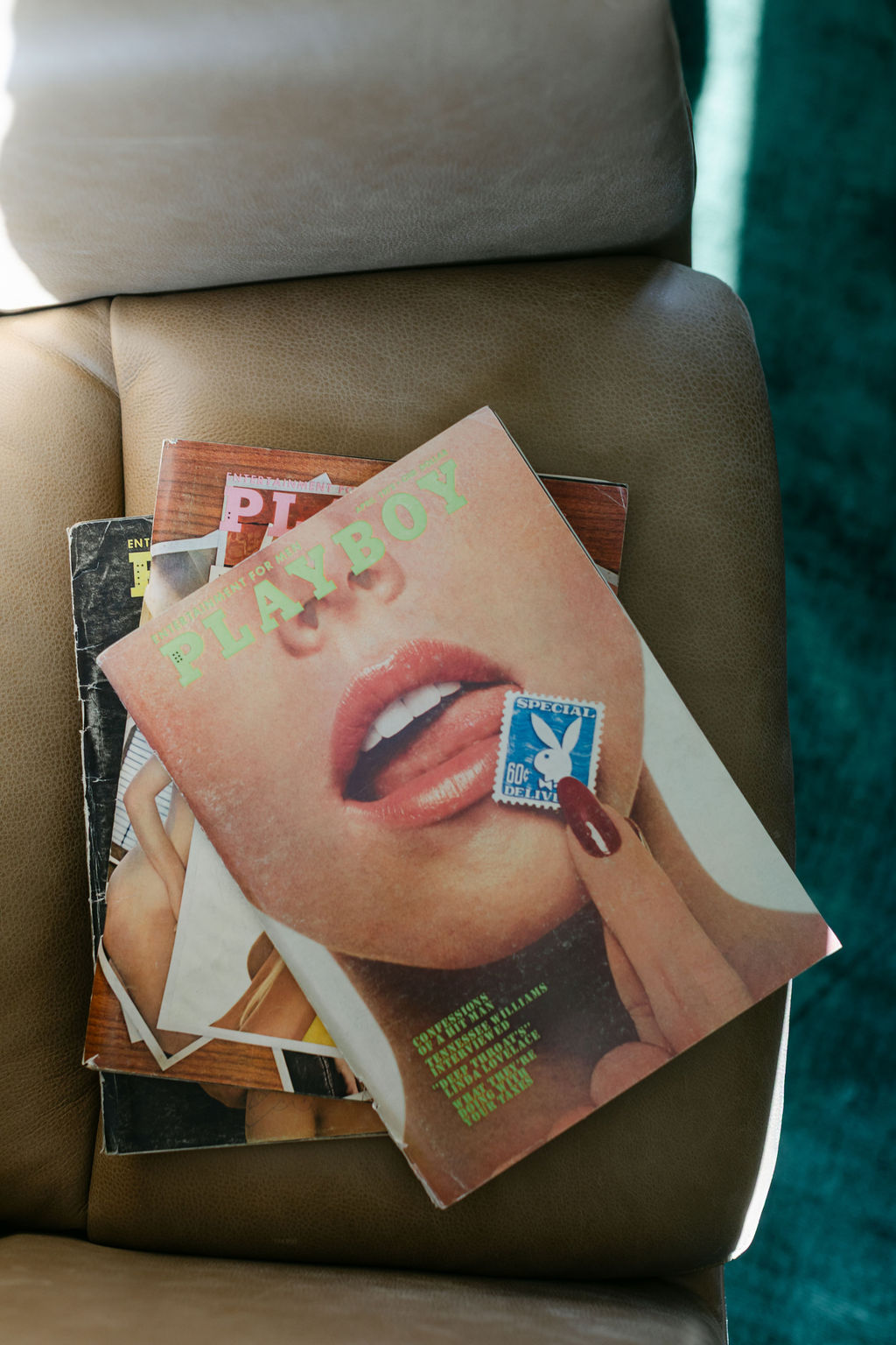 Styled stack of vintage Playboy magazines on a leather chair, adding warmth and personality to a modern interior.