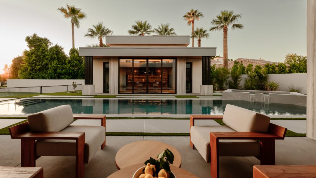 Modern desert backyard with a luxury pool, covered outdoor lounge seating, and a contemporary guest house framed by palm trees, designed by Smyth House.