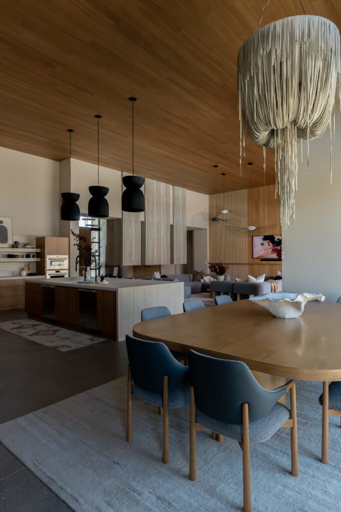 Open-concept living and dining space featuring dramatic sculptural lighting, including oversized black pendants and a cascading fringe chandelier, paired with warm wood ceilings and modern furnishings.