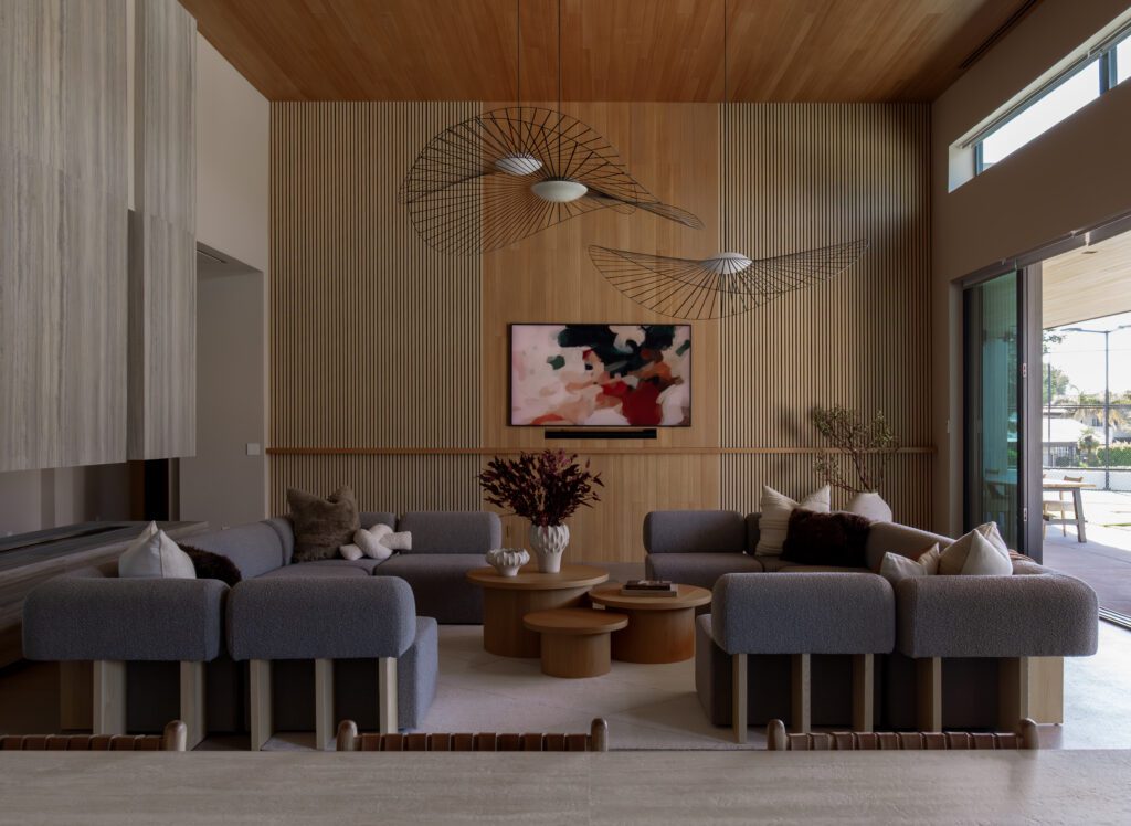 A spacious open-concept living and kitchen area with warm wood ceilings, neutral furnishings, sculptural lighting, and large sliding doors opening to the outdoor space.