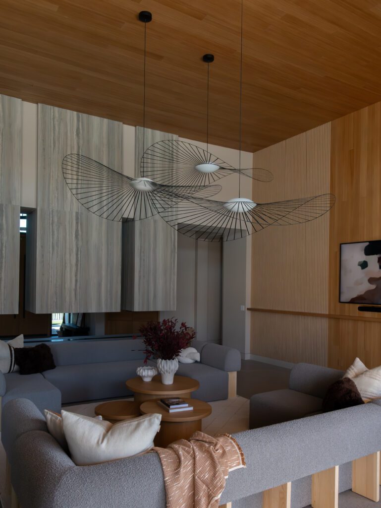 Modern living room with custom gray sectional sofa, warm wood slat feature wall, sculptural ceiling lights, and layered neutral textures designed by Smyth House.