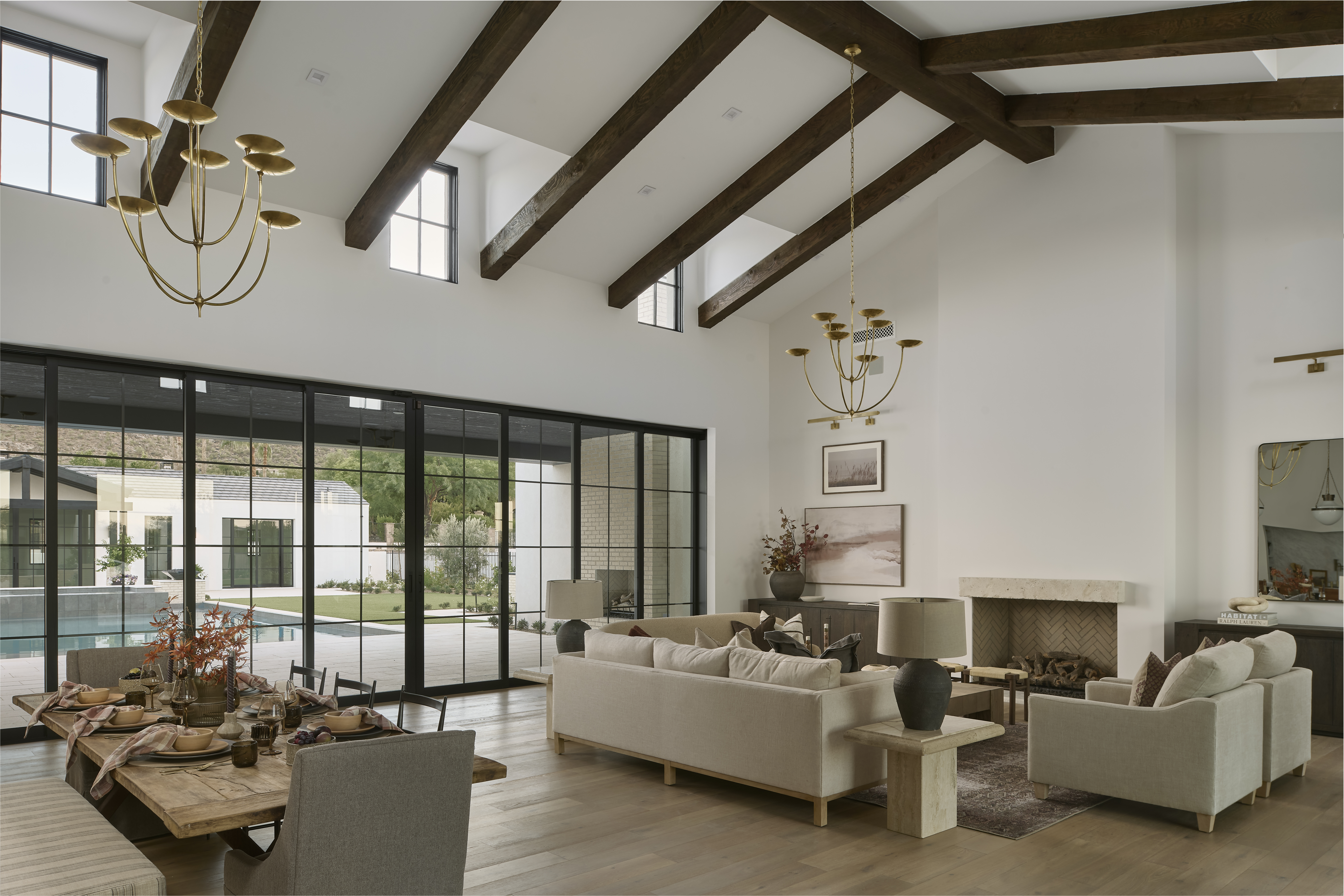 Open-concept living room with exposed wood ceiling beams, steel-framed windows, and layered neutral furnishings designed by Smyth House Interior Design.