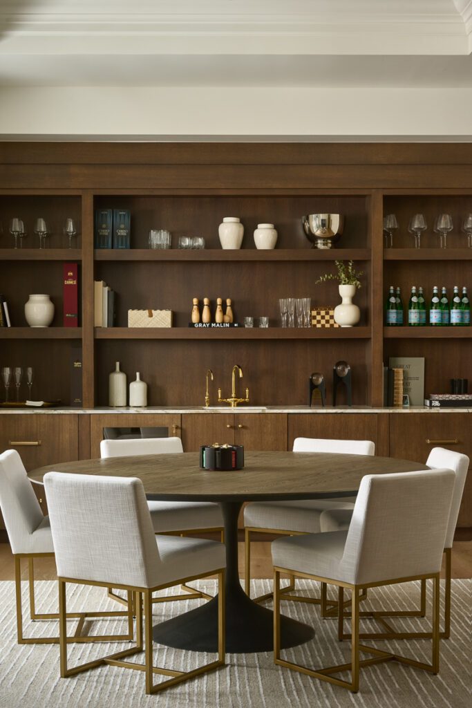 Luxury game room with custom wood shelving, round table seating, and brass accents designed by Smyth House