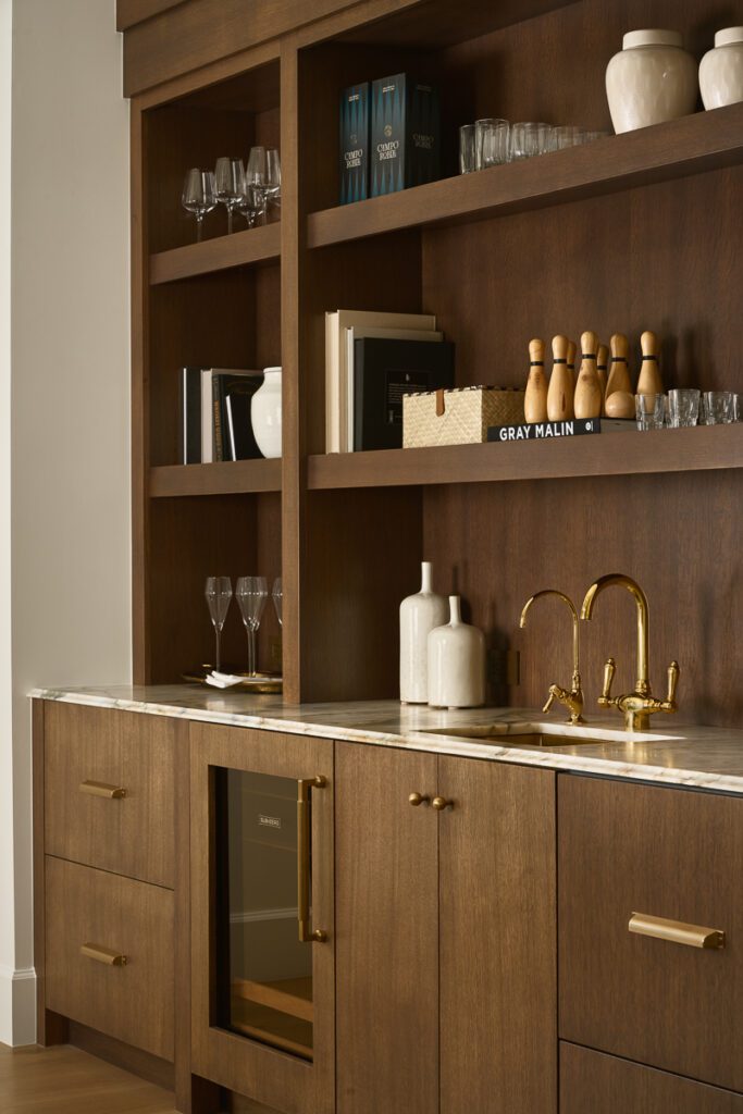 Luxury wet bar with walnut cabinetry, marble countertop, brass faucet, and open shelving