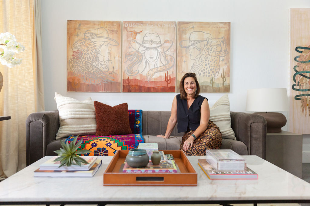 Meredith Smyth, a Luxury interior designer seated on a modern sofa in a styled living room with layered textiles, colorful artwork, and curated coffee table styling, showcasing a cohesive luxury interior design aesthetic.