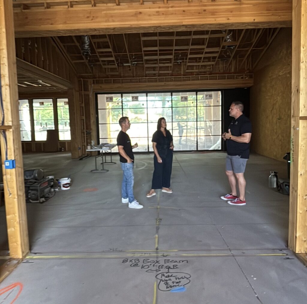 Interior designer and project team standing inside a framed luxury home under construction, reviewing layout and structural elements during the early build phase.