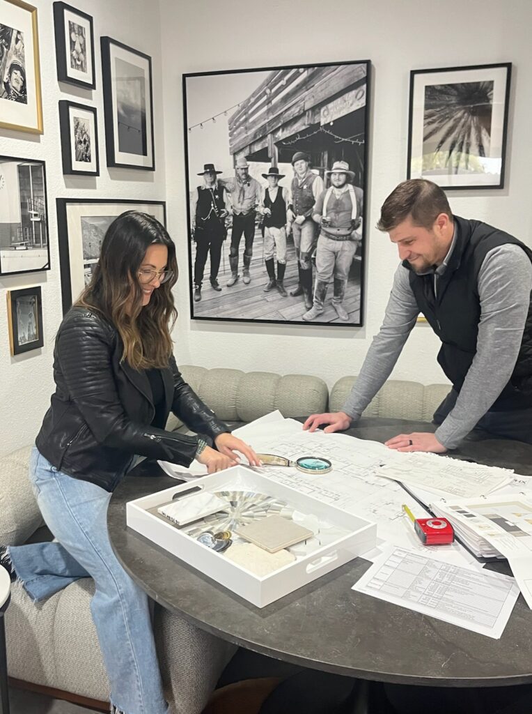 Meredith, Interior designer and client reviewing architectural plans and material samples at a table, collaborating on layout and finish selections in a curated design studio.