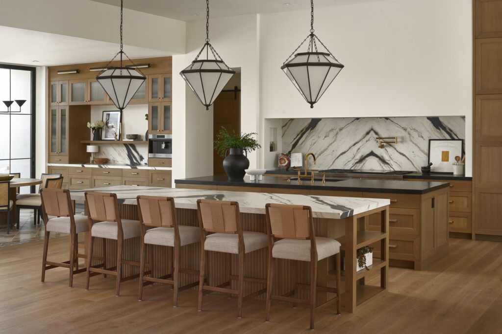 Luxury kitchen interior designed by Smyth House featuring oversized waterfall marble island, warm wood cabinetry, layered lighting, brass fixtures, and seamless open-concept living in a high-end Arizona home.