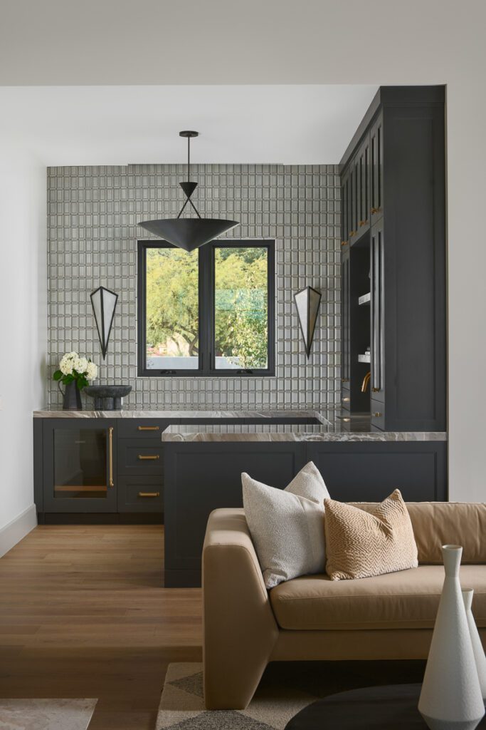 Luxury wet bar and lounge space designed by Smyth House featuring dark custom cabinetry, geometric tile backsplash, brass hardware, dramatic black lighting, and layered textures in a modern Arizona home.
